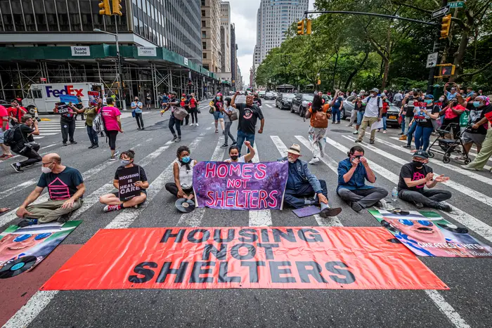 Protesters seen blocking the street behind a banner reading HOUSING NOT SHELTERS at the protest. Members of a NYC homeless advocacy coalition staged a direct action outside City Hall to call out Mayor de Blasios Broken Record on Homelessness.